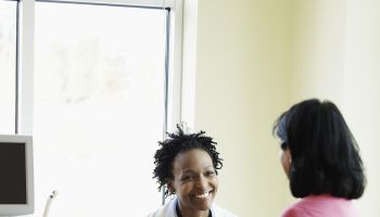 Female doctor talking to woman in exam room, smiling