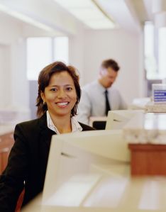 Bank teller smiling, sitting behind computer, portrait