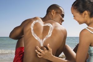 Hispanic woman drawing heart in sunscreen on boyfriend's back