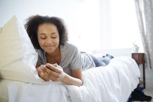 Teenage girl laying on a bed using technology