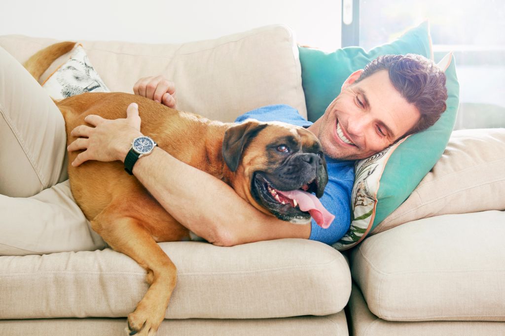 Man lying down cuddling bid dog on the sofa