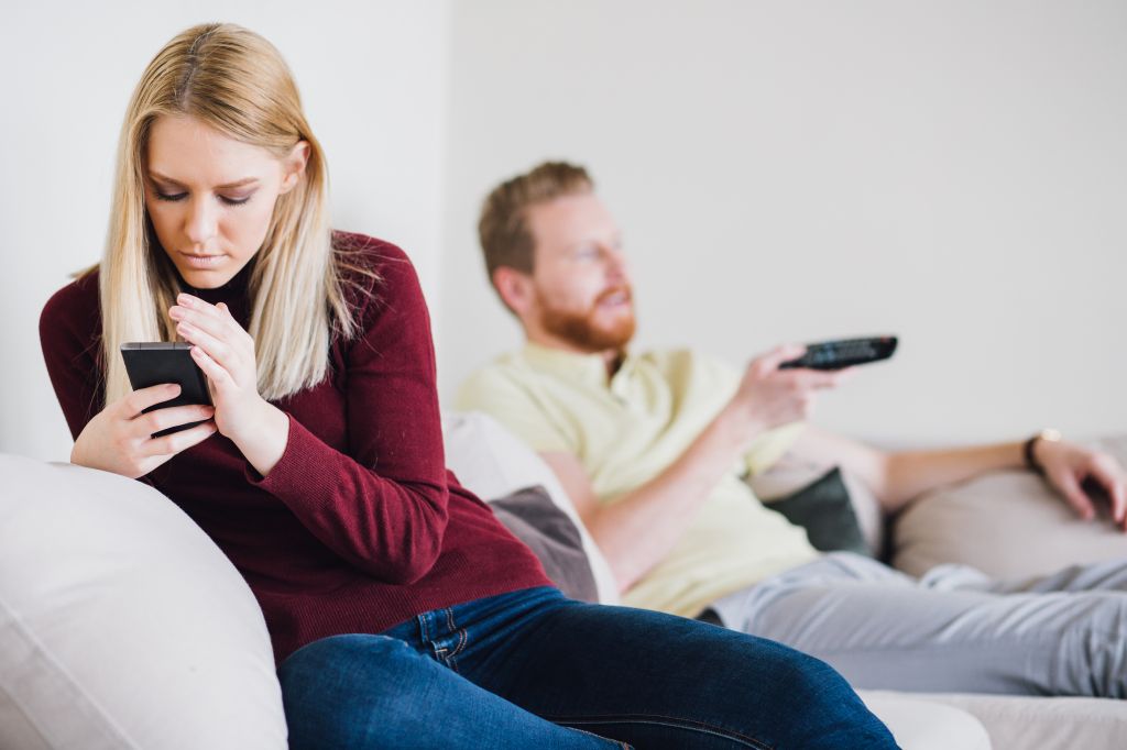 Woman using phone and hiding it from the man on the other side of sofa bed