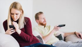 Woman using phone and hiding it from the man on the other side of sofa bed