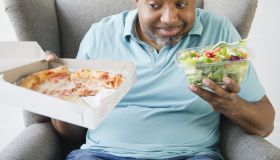 African American deciding between salad and pizza