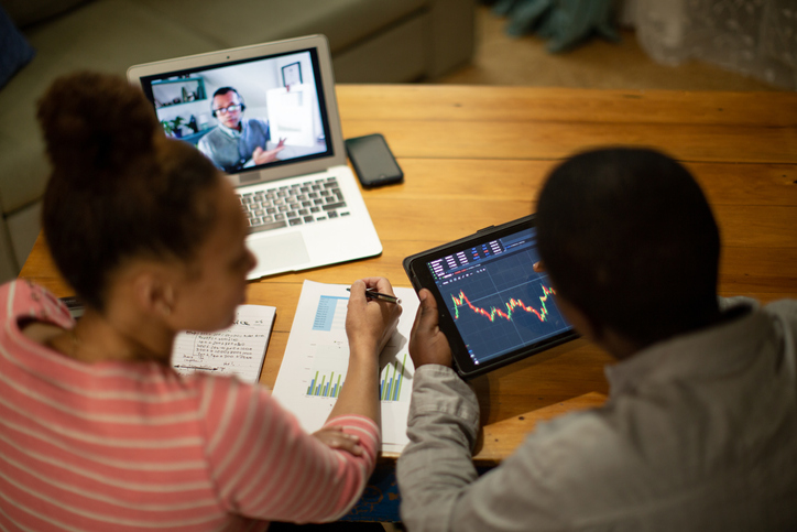 Couple discussing stock market trading on a videocall with a financial consultant from their home
