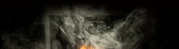 Close up laptop burned with flame and smokes on a wooden desk isolated over black background.