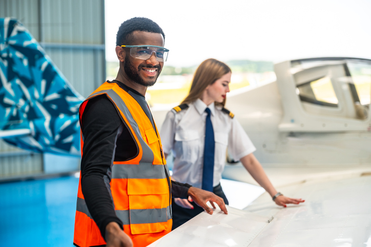 Aircraft maintenance engineer and pilot inspecting airplane wing in hangar