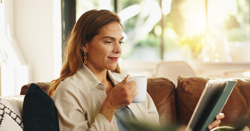 Tablet, coffee and woman relax in home for streaming movie, show and watch drama online. Technology, happy person and drink while reading ebook on internet, news and check social media on weekend