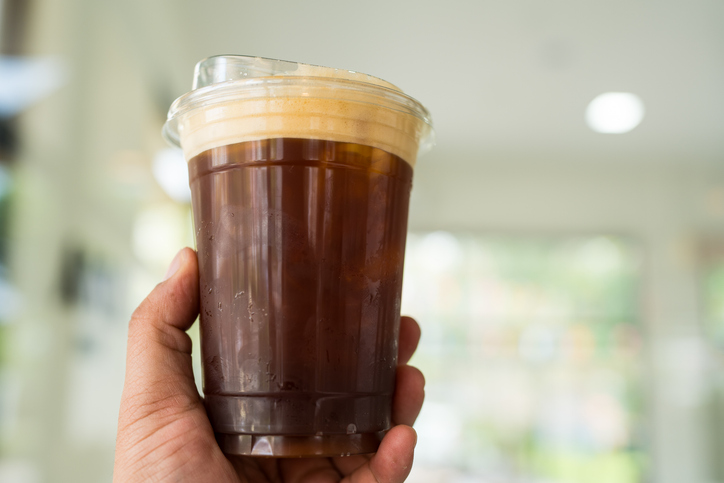 Hand gripping a glass of cold black coffee with a cafe.