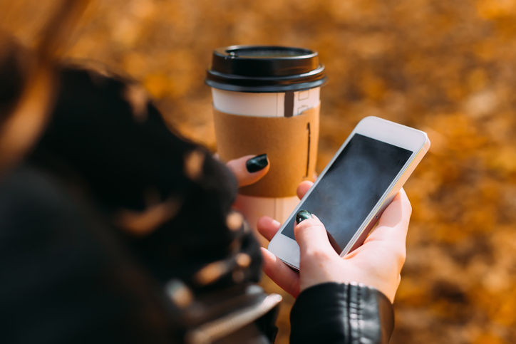 Close-up of a paper cup with coffee and a cellphone in the hands