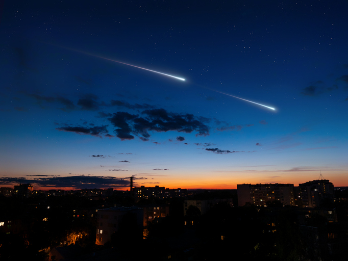 Meteor trails in the sky over the city. Magical night with falling stars.