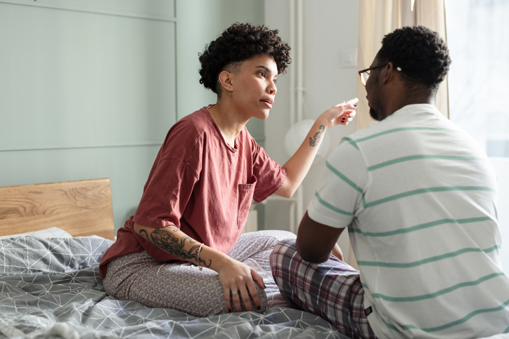 A tense moment between a couple in a bedroom, sitting on a bed, expressing conflict and emotion during a disagreement