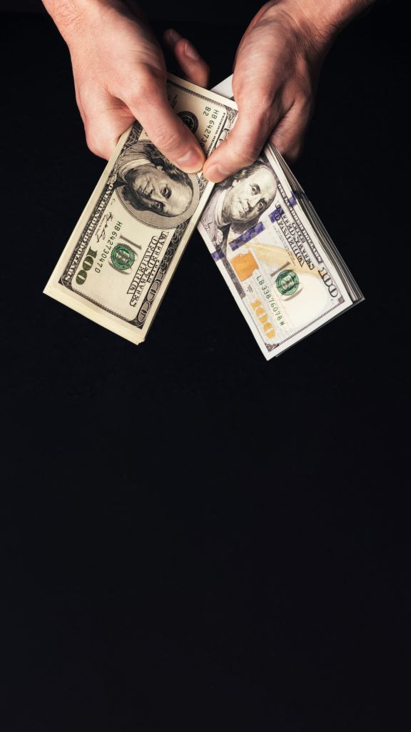 Man hand holding two stacks of US hundred dollar bill against black background, old and new design