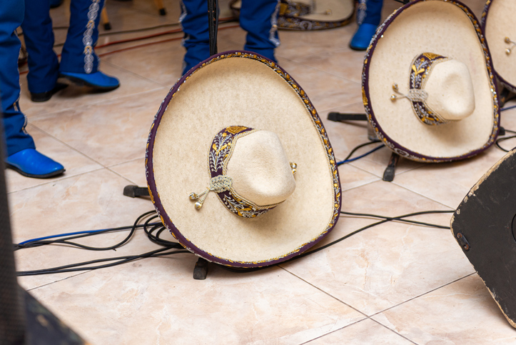 A beautifully decorated mariachi sombrero sits on a stand alongside a mariachi performer in bright blue boots