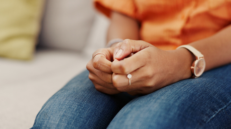 Hands, nervous and woman on sofa, home and anxiety with concern, stress and worry. Apartment, fear and person with depression, mental health and sad in living room for grief, loss and emotional