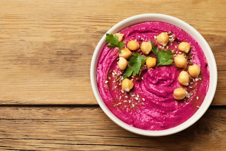 Tasty beet hummus with chickpeas and parsley in bowl on wooden table, top view. Space for text
