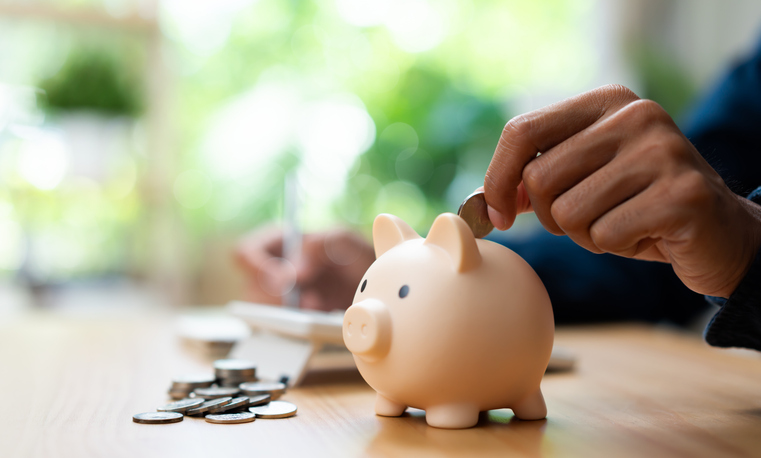 Piggy bank savings concept with close up hand putting coin into money box, representing banking, cash savings, financial planning, and personal wealth management.