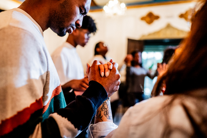 Young man praying together with other worshippers around her during a religious service