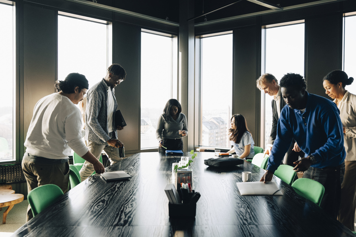 Group of diverse coworkers gathering around long black table for meeting in office
