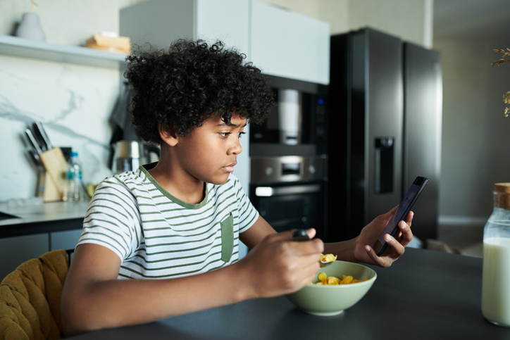 Young Boy Having Breakfast While Using Smartphone