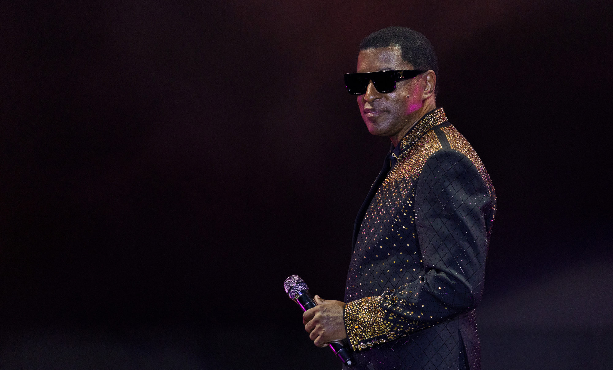 A man wearing sunglasses and a sparkling gold and black outfit performing on stage at the Soul Beach Music Festival.