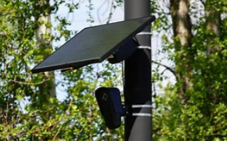 Solar-powered security camera mounted on a pole in a wooded area.