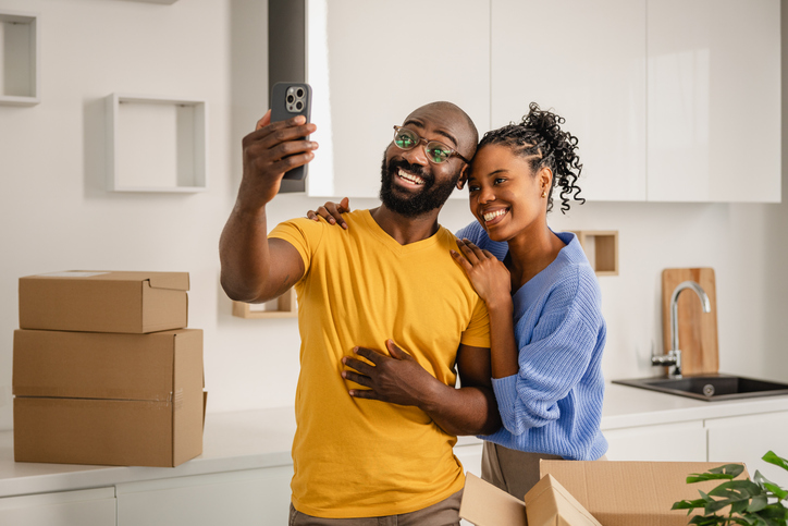 Young couple taking selfie in new kitchen surrounded by moving boxes