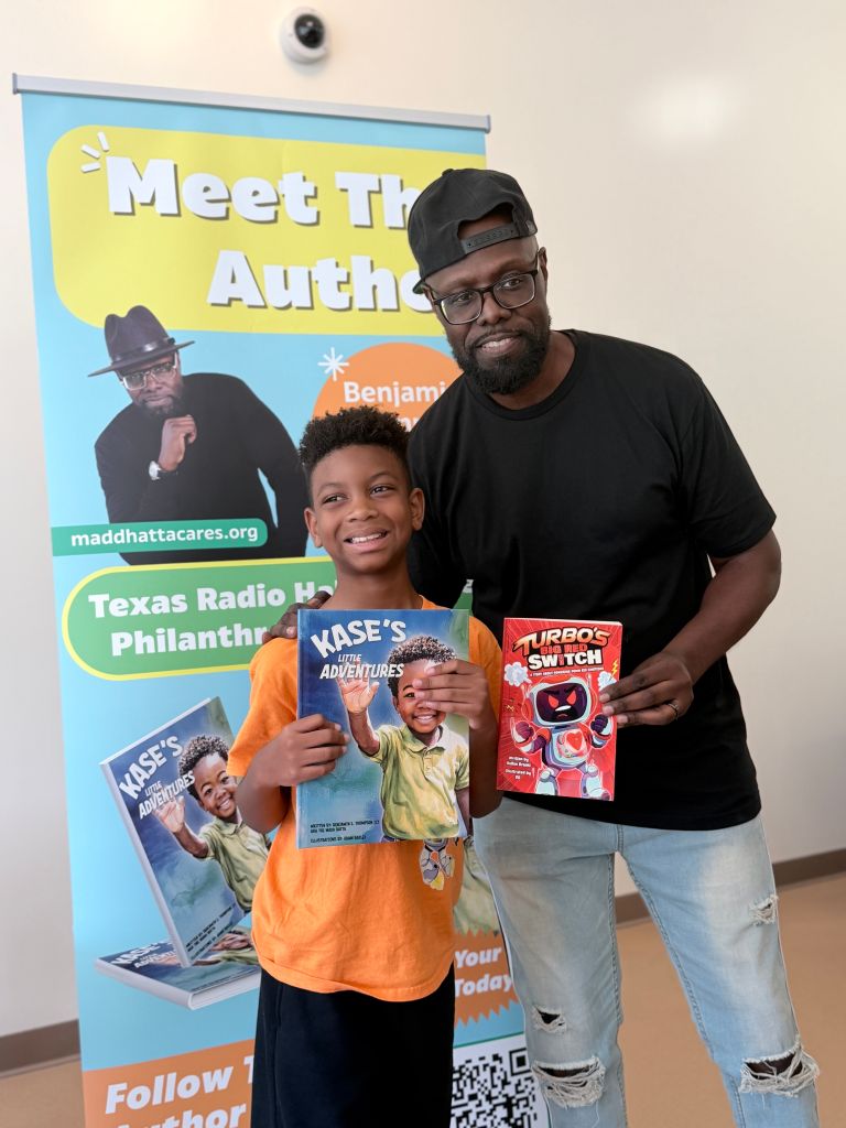 A smiling young boy holding books stands next to a bearded man in a black t-shirt in front of a "Meet the Author" banner for "Kase's Adventures" and "Turbos Switch" books.